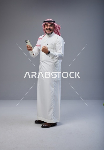 رجل سعودي بالزي التقليدي يحتفل مع هاتف ذكي
