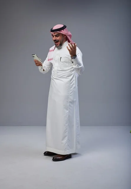 رجل سعودي يرتدي الثوب التقليدي يستخدم الهاتف في الاستوديو