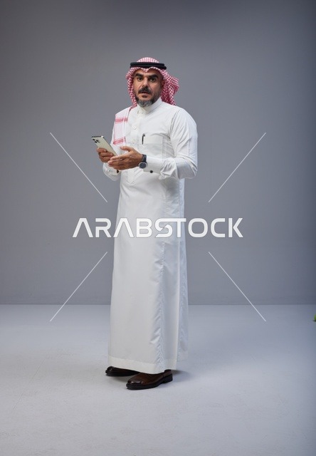 رجل سعودي بالزي التقليدي يستخدم الهاتف الذكي
