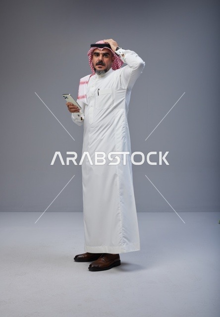 رجل سعودي بالزي التقليدي يمسك هاتف ذكي