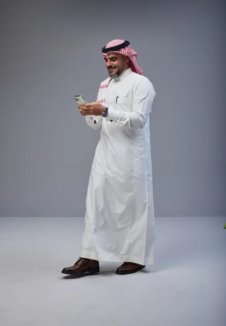 Saudi Man in Traditional Thobe Using Phone While Walking