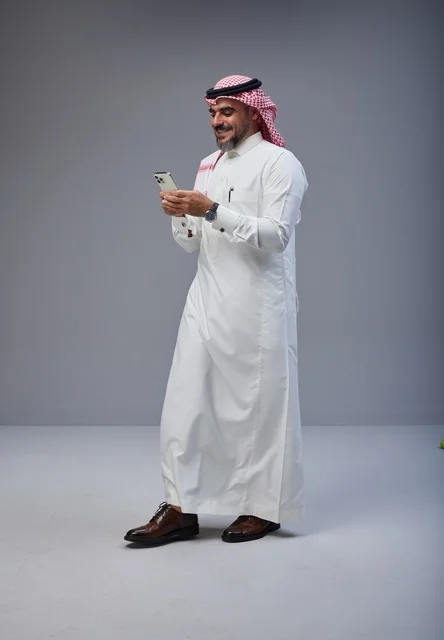رجل سعودي بالزي التقليدي يستخدم الهاتف أثناء المشي