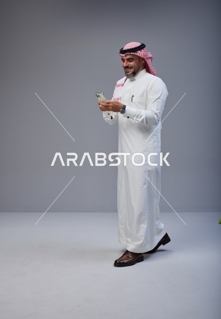 رجل سعودي بالزي التقليدي يستخدم الهاتف أثناء المشي