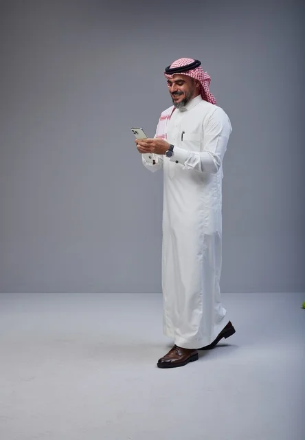 رجل سعودي بالزي التقليدي يستخدم الهاتف أثناء المشي