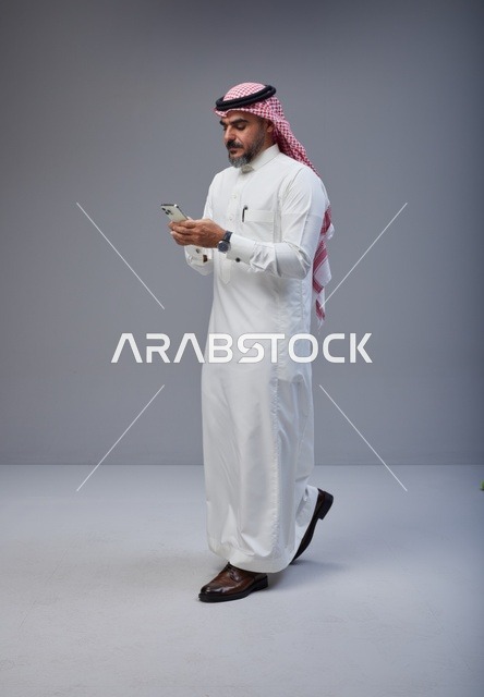 Saudi Man in Traditional Thobe Using Smartphone Walking