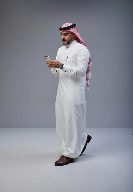 Saudi Man in Traditional Thobe Using Smartphone Walking