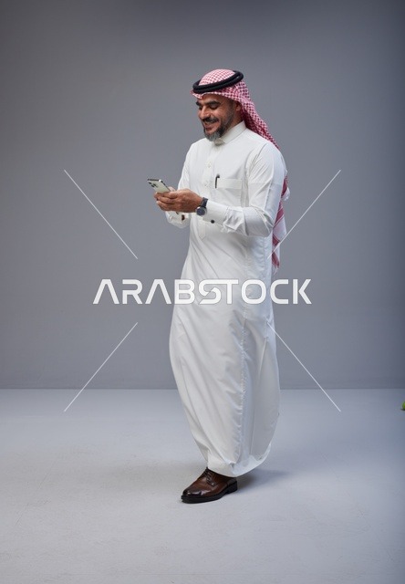 رجل سعودي بالزي التقليدي يستخدم الهاتف أثناء المشي