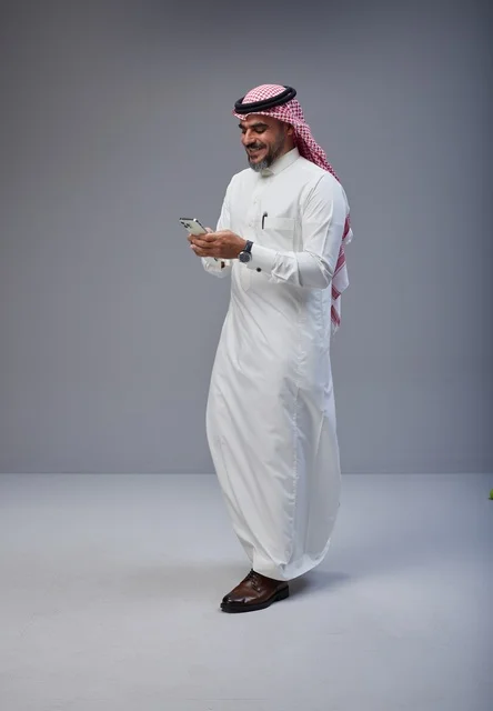 رجل سعودي بالزي التقليدي يستخدم الهاتف أثناء المشي