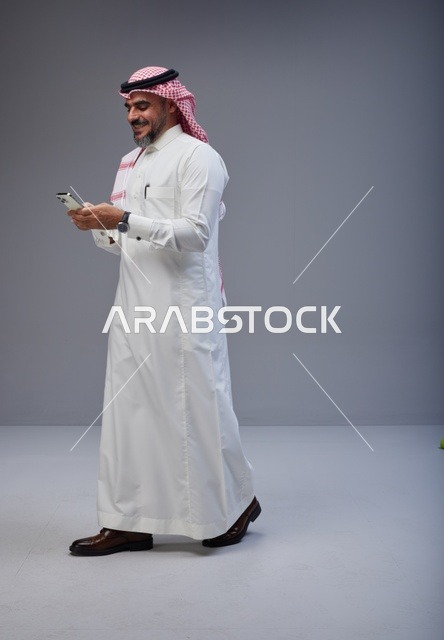 رجل سعودي بالزي التقليدي يستخدم الهاتف أثناء المشي