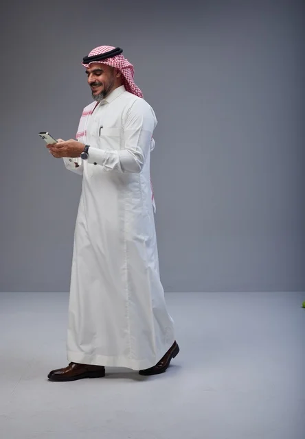 Saudi Man in Traditional Thobe Using Phone While Walking