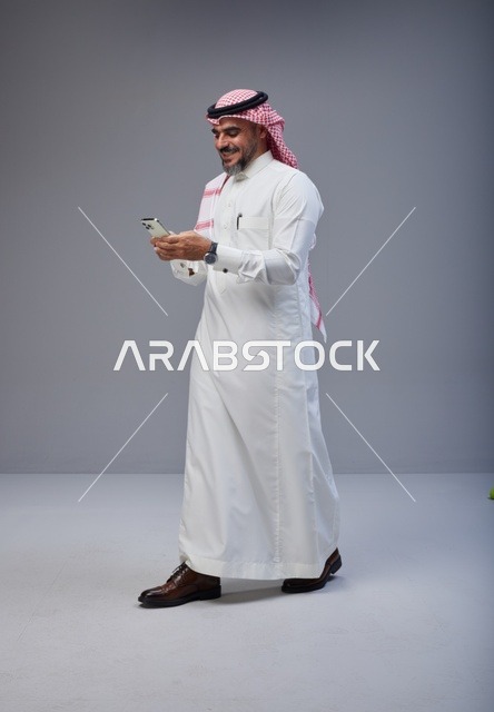 رجل سعودي بالزي التقليدي يستخدم الهاتف أثناء المشي