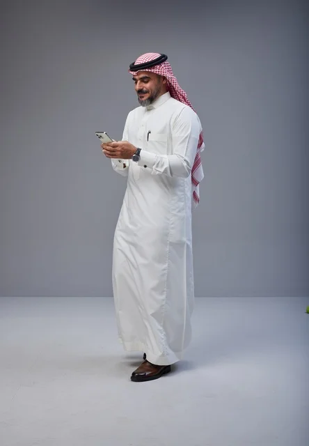 Saudi Man in Traditional Thobe Using Phone While Walking