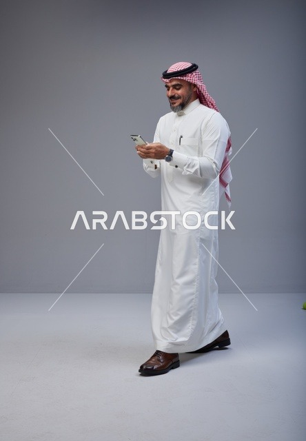 Saudi Man in Traditional Thobe Using Phone Walking