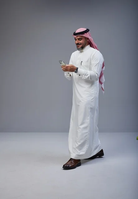 Saudi Man in Traditional Thobe Using Phone Walking