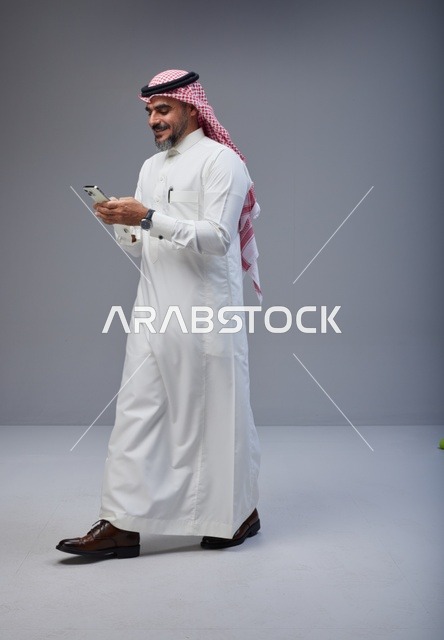 Saudi Man in Traditional Thobe Using Phone while Walking