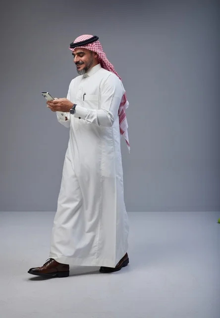 رجل سعودي بالزي التقليدي يستخدم الجوال أثناء المشي