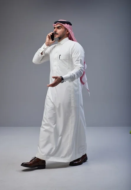 Saudi man in traditional attire talking on smartphone