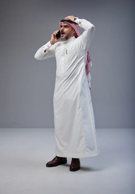 رجل سعودي بالزي التقليدي يتحدث عبر الهاتف بصدمة