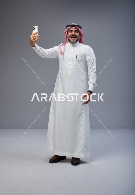 رجل سعودي بالزي التقليدي يلتقط صورة سيلفي في استوديو