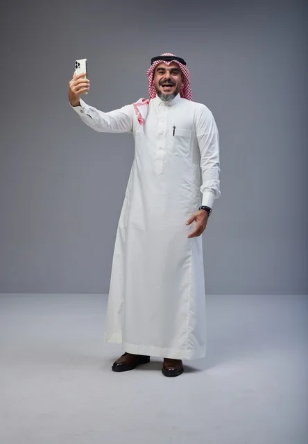 رجل سعودي بالزي التقليدي يلتقط صورة سيلفي في استوديو