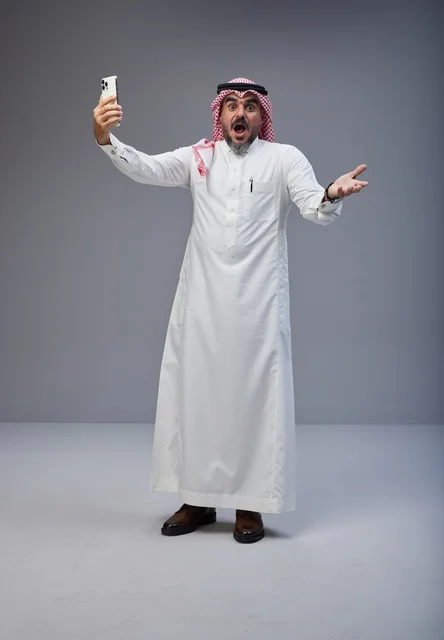 رجل سعودي بالزي التقليدي مندهش يمسك هاتف ذكي