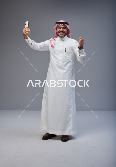 رجل سعودي بالزي التقليدي يلتقط صورة سيلفي بالجوال