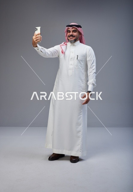 رجل سعودي بالزي التقليدي يلتقط صورة سيلفي في الاستوديو