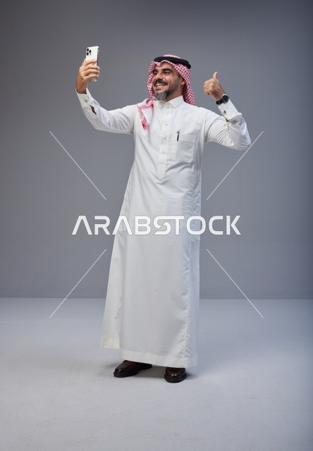 رجل سعودي بالزي التقليدي يلتقط سيلفي مع إشارة الإعجاب