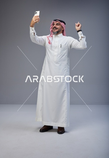 رجل سعودي بالزي التقليدي يلتقط صورة سيلفي بالجوال