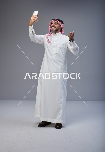 رجل سعودي بالزي التقليدي يلتقط صورة سيلفي في استوديو