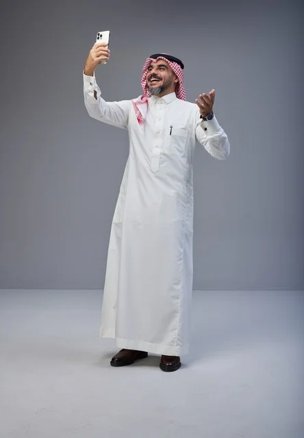 رجل سعودي بالزي التقليدي يلتقط صورة سيلفي في استوديو