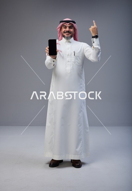 رجل سعودي يحمل هاتف ذكي ويشير للأعلى في استوديو
