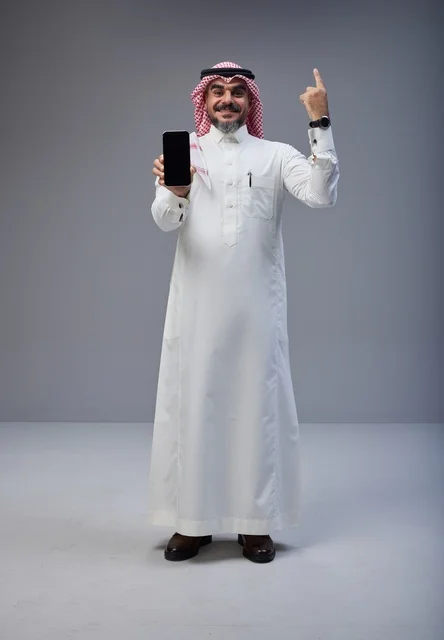 رجل سعودي يحمل هاتف ذكي ويشير للأعلى في استوديو