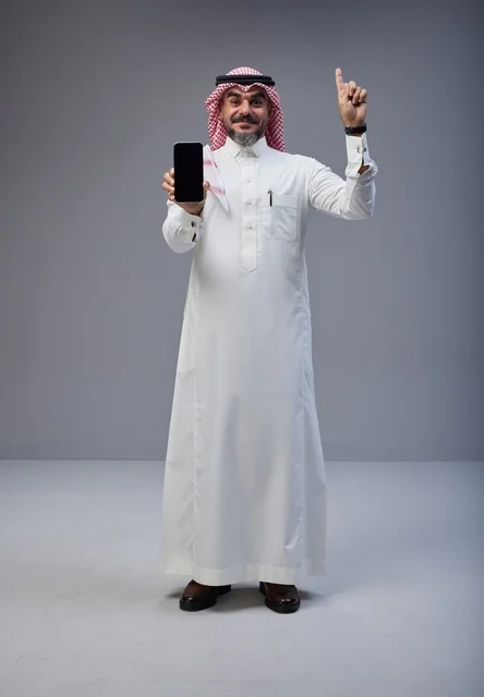 رجل سعودي بالزي التقليدي يحمل هاتف ذكي ويشير للأعلى