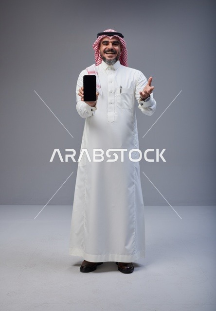 رجل سعودي بالزي التقليدي يحمل هاتف ذكي بشاشة فارغة