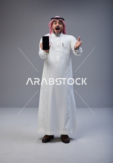 رجل سعودي بالزي التقليدي يحمل هاتف ذكي في استوديو