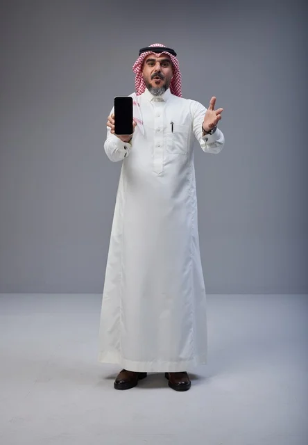Saudi Man in Traditional Dress Holding Smartphone Studio