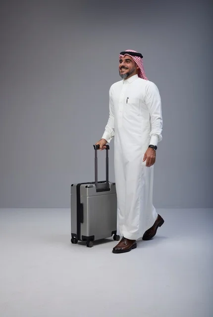 رجل سعودي بالزي التقليدي يمشي مع حقيبة سفر في الاستوديو