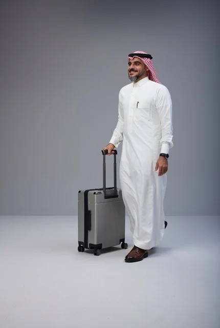 رجل سعودي بالزي التقليدي يمشي مع حقيبة سفر في استوديو