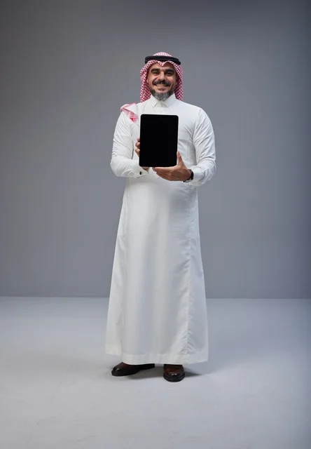رجل سعودي بالزي التقليدي يحمل جهاز لوحي بشاشة فارغة