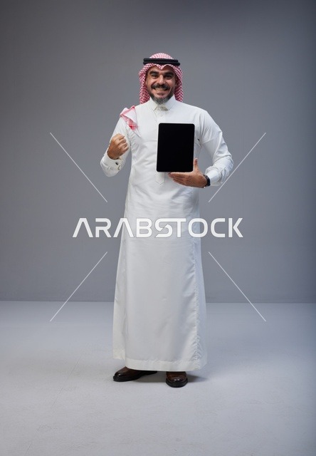 رجل سعودي يحمل جهاز لوحي بشاشة فارغة في الاستوديو