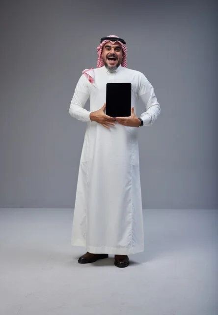 رجل سعودي بالزي التقليدي يحمل جهاز لوحي بشاشة فارغة