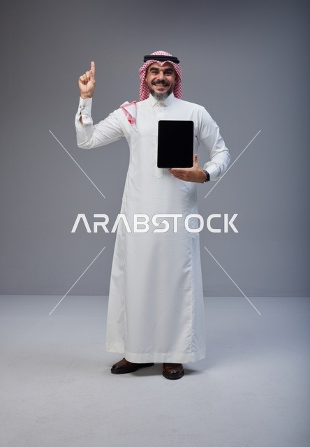 رجل سعودي يحمل جهاز لوحي بشاشة فارغة في الاستوديو