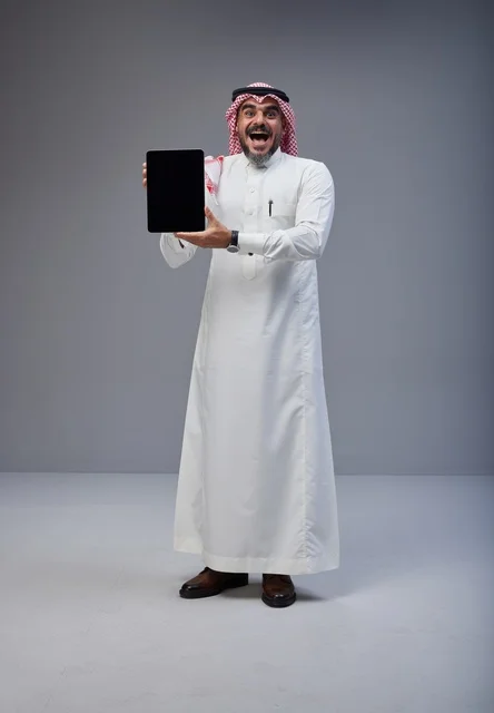 رجل سعودي بالزي التقليدي يحمل جهاز لوحي بشاشة فارغة