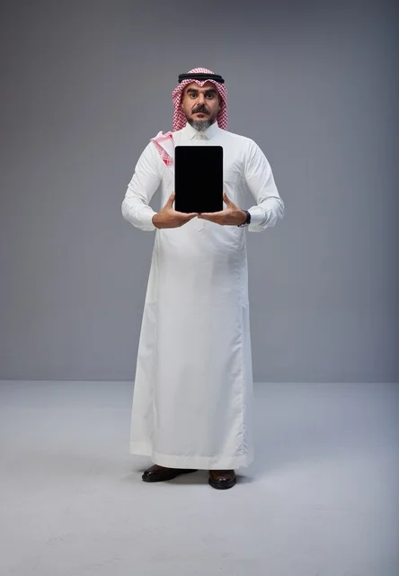 رجل سعودي بالزي التقليدي يحمل جهاز لوحي بشاشة فارغة