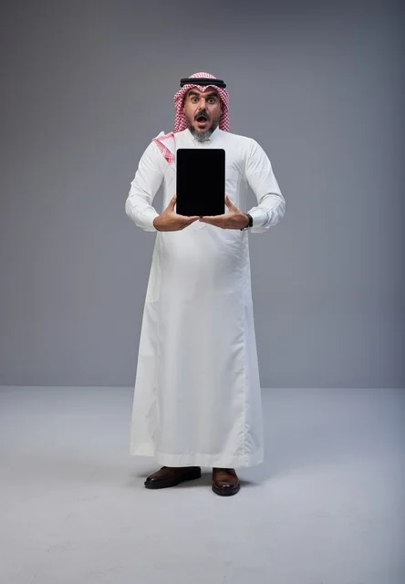 رجل سعودي يحمل جهاز لوحي بتعبير وجه مندهش