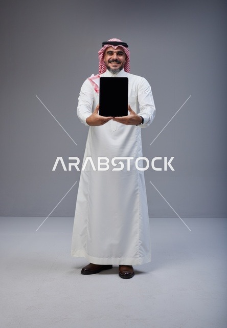 رجل سعودي يحمل جهاز لوحي بشاشة فارغة في الاستوديو