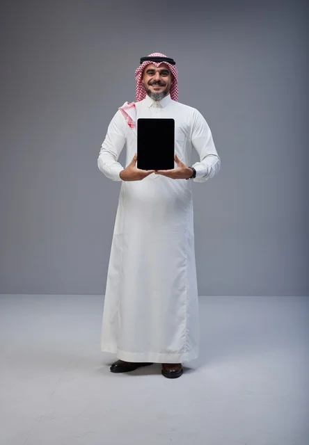 رجل سعودي بالزي التقليدي يحمل جهاز لوحي بشاشة سوداء