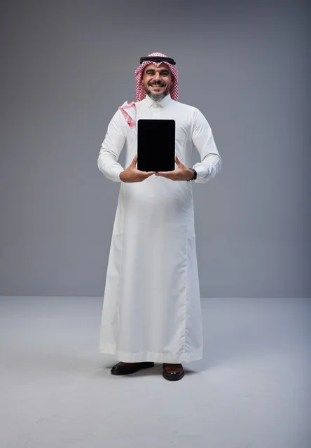 رجل سعودي بالزي التقليدي يحمل جهاز لوحي شاشة فارغة