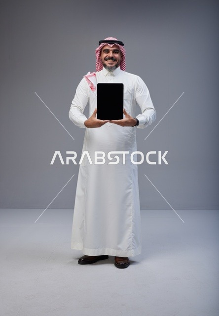 رجل سعودي بالزي التقليدي يحمل جهاز لوحي شاشة فارغة